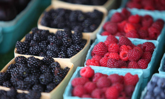 Paper berry baskets full of freshly-picked blackberries, raspberries, and blueberries sit on a display table.