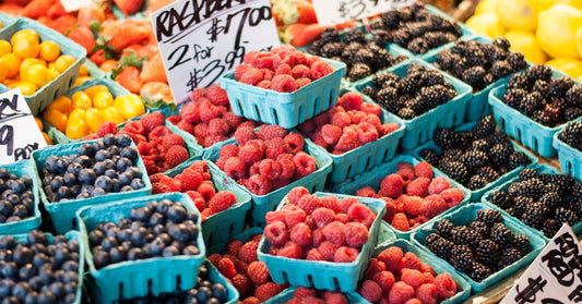 Rows of fresh berries in paper berry boxes sit on display. A handwritten sign reads "Raspberry, 2 for $7.00 or $3.99."