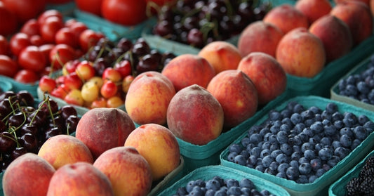 Turquoise containers are filled with fruits, including cherries, peaches, blueberries, blackberries, and tomatoes.