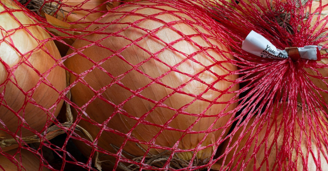 A red mesh bag holds eight large yellow onions. It's tied with a small white tag with black text at one end.