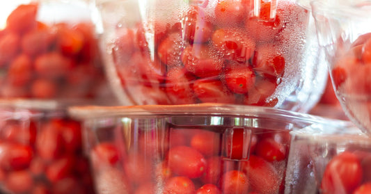 Six clear plastic containers hold firm, red cherry tomatoes with shiny skins and visible condensation on the inside.