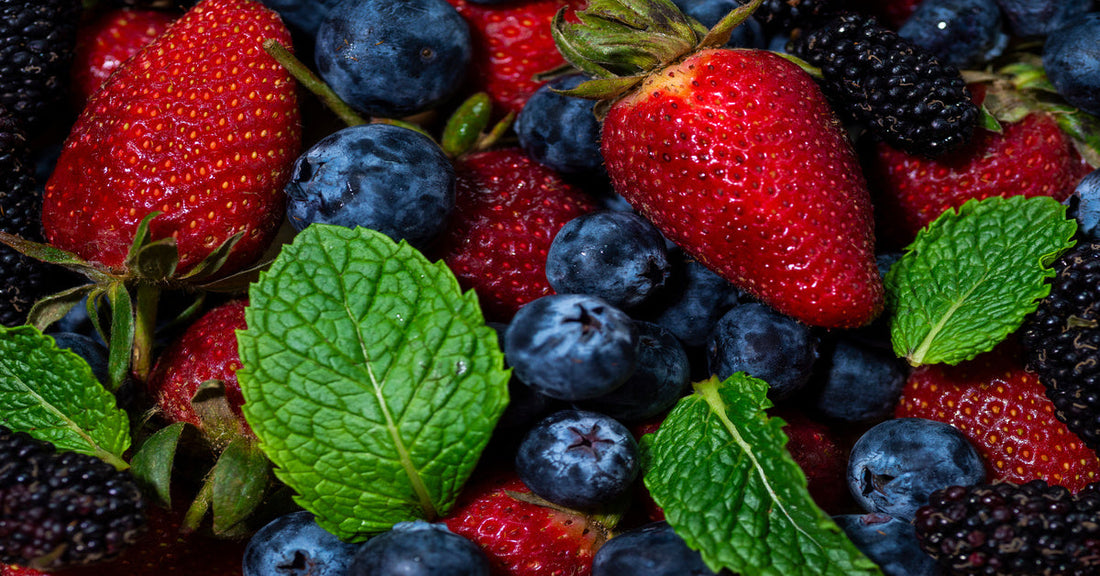 A close-up view of fresh strawberries, blueberries, blackberries, and leaves laying in a pile together.