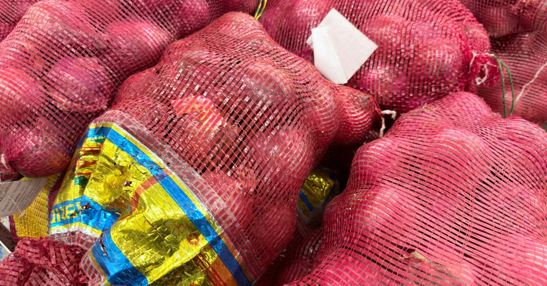 Stacks of red onions fill red mesh produce bags. The stacks are piled closely together with a gold and blue label on one bag.