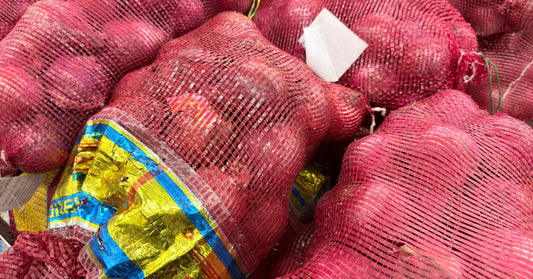 Stacks of red onions fill red mesh produce bags. The stacks are piled closely together with a gold and blue label on one bag.