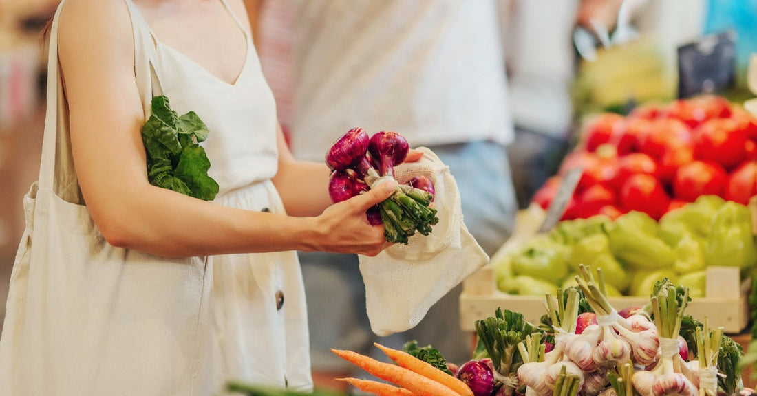 A woman surrounded by colorful vegetables and produce holds a bunch of fresh radishes at a farmers market.