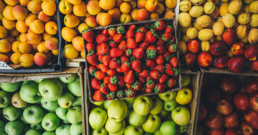 A cardboard box holds bright strawberries among boxes of apricots, green apples, and other fruit for sale.